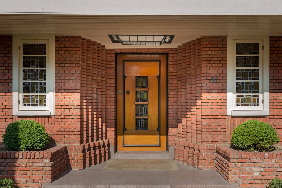Porte d'entrée en bois avec vitrage artistique, façade en briques rouges, architecture élégante, accueillante, design moderne, ANTE Festival Bruxelles, espace culturel.